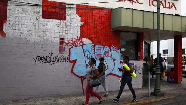Pedestrians walk past a building tagged with graffiti a day after Puerto Rican Governor Alejandro Garcia Padilla gave a televised speech regarding the governments $72 billion debt on June 30, 2015.
